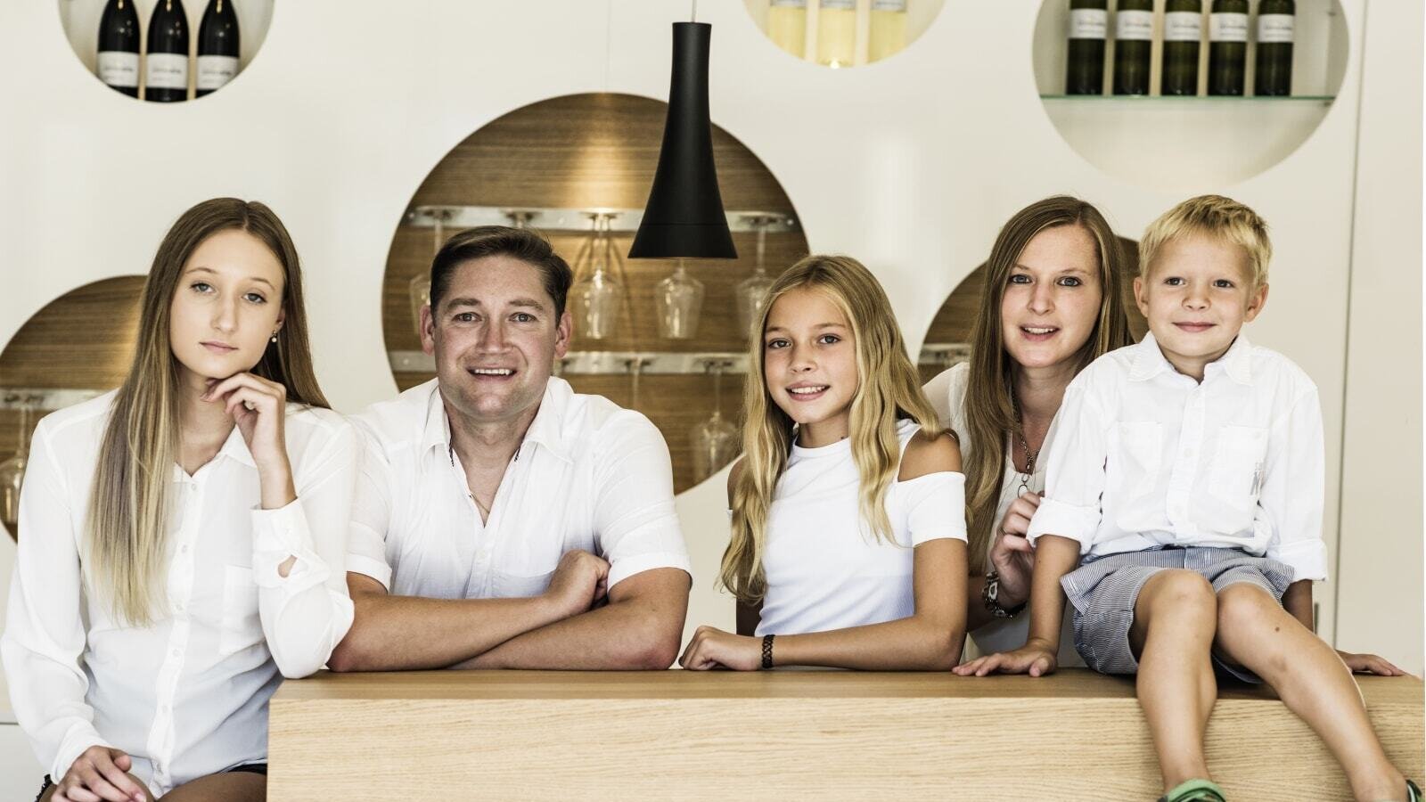 The family who operates the farmhouse, standing behind a wooden counter with wine bottles and glassware on display.