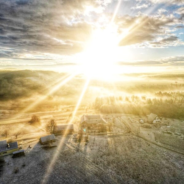 Aerial view of the Farm House and the surrounding frosty rural landscape with sunlight and fog.