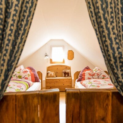 A cozy, rustic bedroom in the farmhouse featuring two wooden single beds with colorful floral bedding under a sloped ceiling.