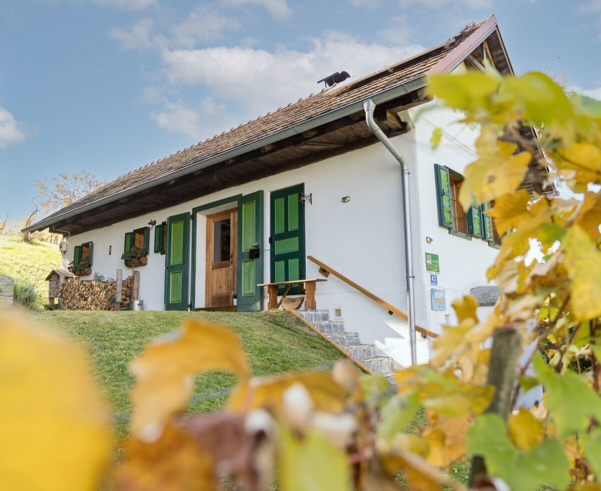 The inviting farmhouse with traditional green shutters, set on a grassy hill and framed by warm autumn leaves.