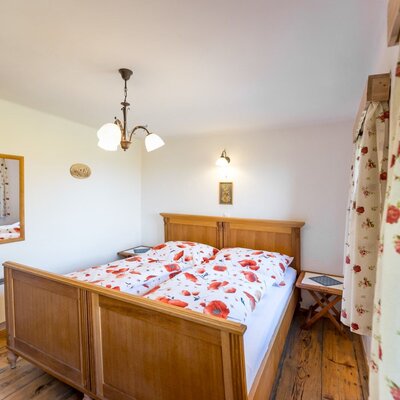 A cozy bedroom in the farmhouse featuring a wooden double bed with playful poppy-patterned bedding and warm lighting.