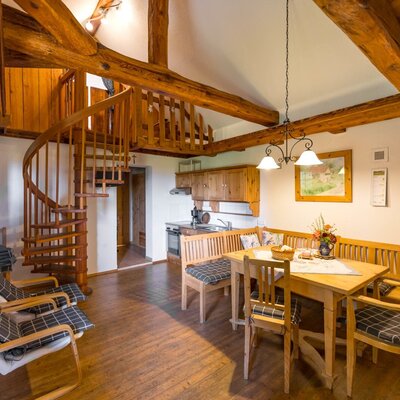 The farmhouse's cozy lounge featuring rustic wooden ceiling beams, an inviting dining area, and a striking spiral staircase.