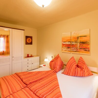 Bedroom in the farmhouse with a double bed, orange bedding, white wardrobe with mirror, and nightstands.