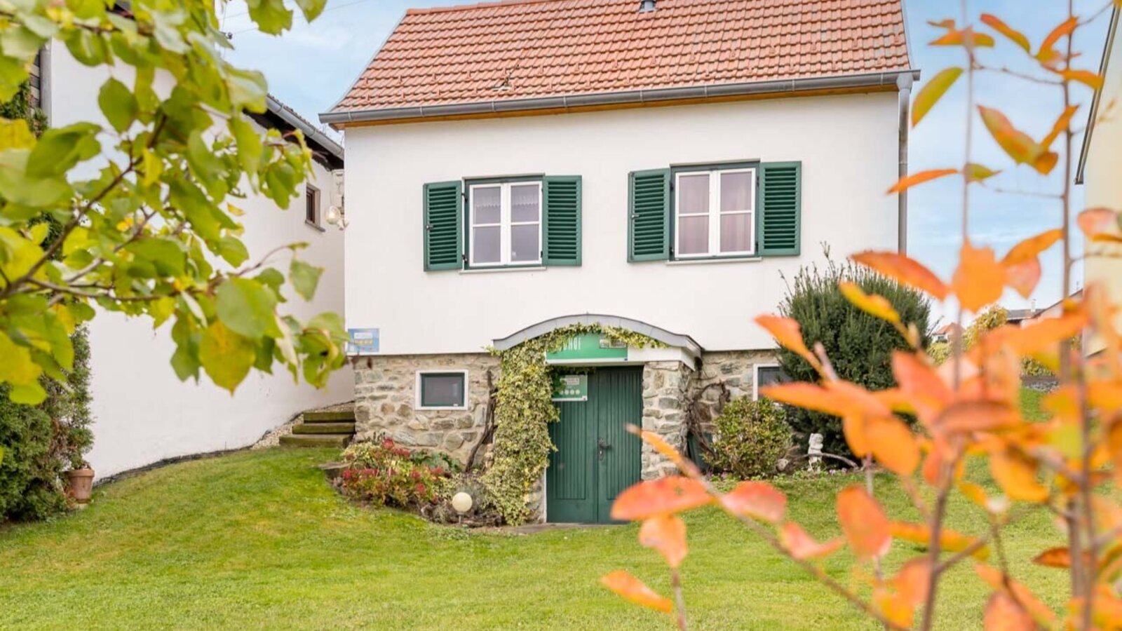 Exterior view of the Bauernhof, featuring a white building with a red tiled roof, green shutters, and a grassy lawn in the foreground.