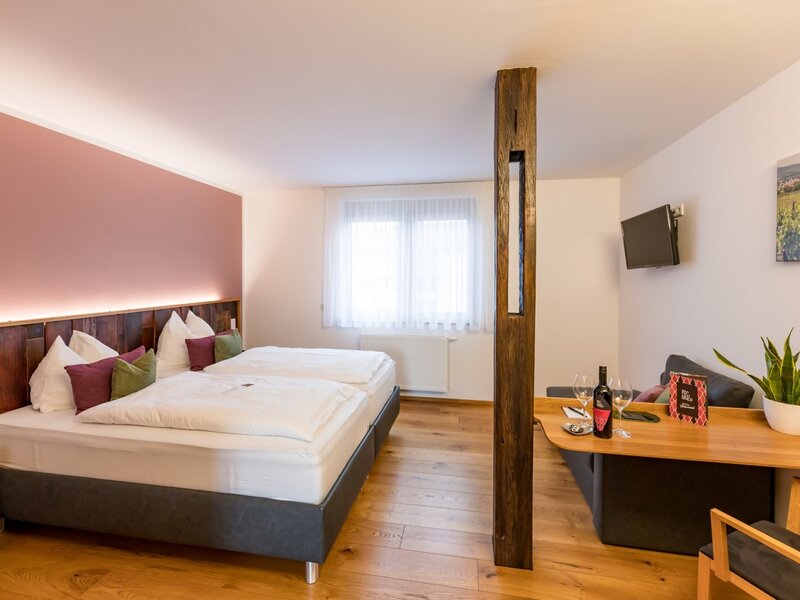 A bedroom in the farmhouse featuring two single beds, a wooden headboard, a window, and a seating area with a sofa, table, and wall-mounted TV.