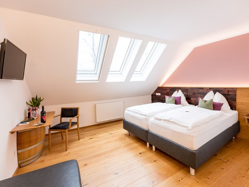 Bedroom in the farmhouse with two single beds, three skylight windows, a wall-mounted TV, and a wooden barrel-style table with a chair.