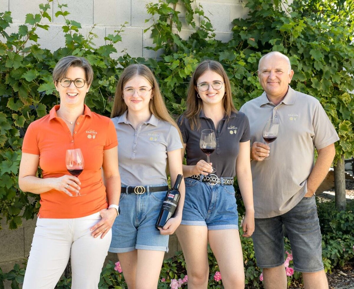 The farmhouse team presents their wine, standing in front of grapevines.