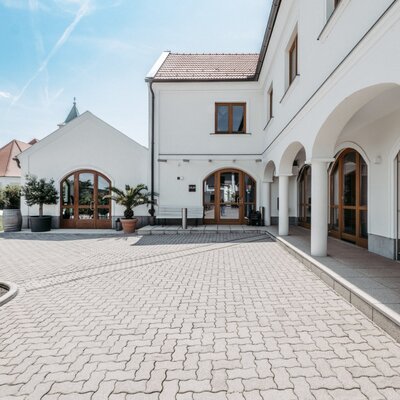 The entrance and paved courtyard of the farmhouse, featuring white buildings with arched wooden doors.