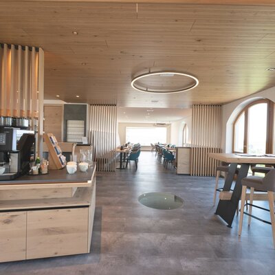 The self-service coffee machine in the lounge area of the farmhouse, featuring dining tables, bar seating, and arched windows.