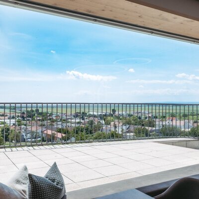Balcony at the farmhouse with tiled flooring and a metal railing, offering views of the village and distant fields.
