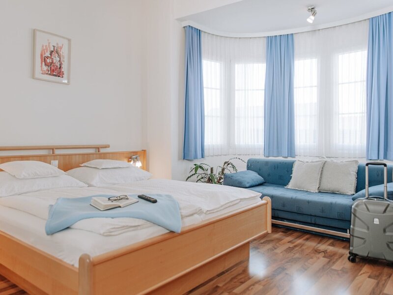 Bedroom in the Haus with a double bed, a sofa, and windows with blue curtains.
