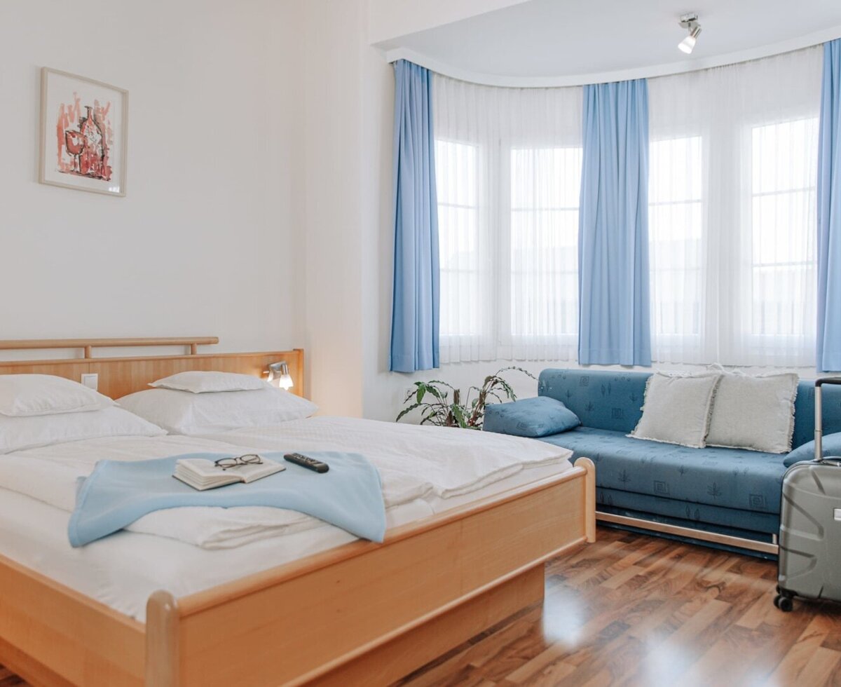 Bedroom in the Haus with a double bed, a sofa, and windows with blue curtains.