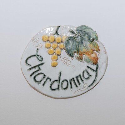 A round ceramic sign featuring the word 'Chardonnay' and a relief of grapes and a leaf in the Haus.