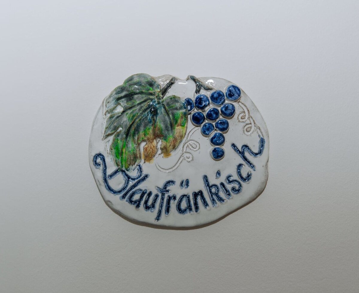 Ceramic plaque in the Haus featuring 'Blaufränkisch' lettering, a grape cluster, and a vine leaf design.