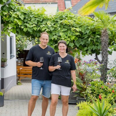 The owners of the farmhouse holding glasses of wine in the property's lush courtyard garden.