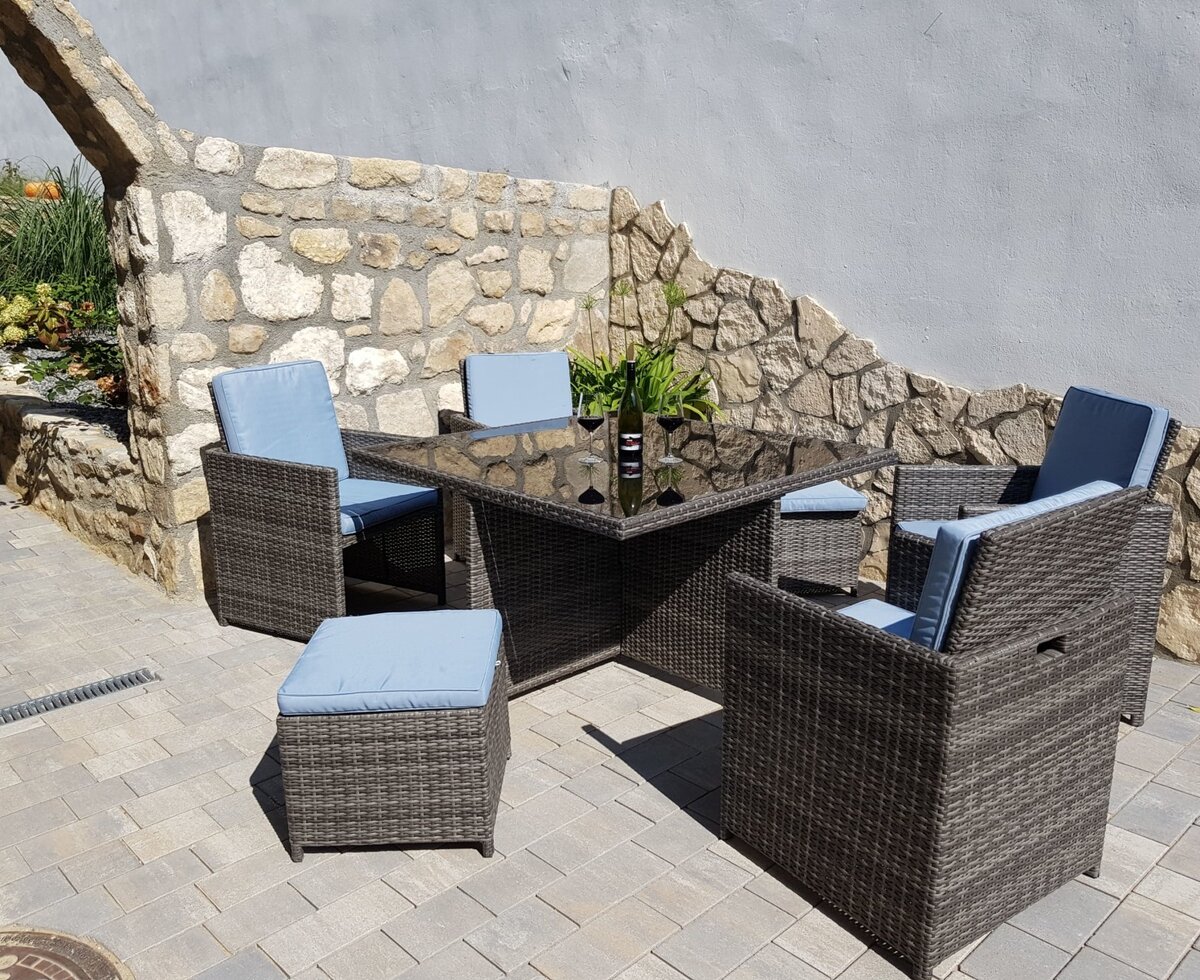 Outdoor seating area at the farmhouse featuring a square table, four chairs with blue cushions, and an ottoman on a paved patio.