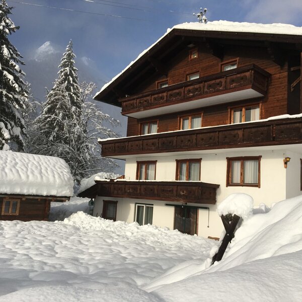 The farmhouse exterior in winter, featuring traditional wooden balconies and a snow-covered landscape.