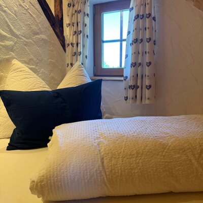 A cozy sleeping area in the Alm featuring plush bedding and a charming small window with patterned curtains.