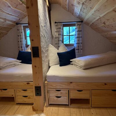 A cozy bedroom in the Alm featuring rustic wooden beds under a sloped ceiling with integrated storage drawers.