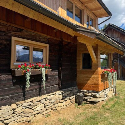 The charming exterior of the Alm, featuring traditional wooden walls, a natural stone foundation, and blooming window boxes.