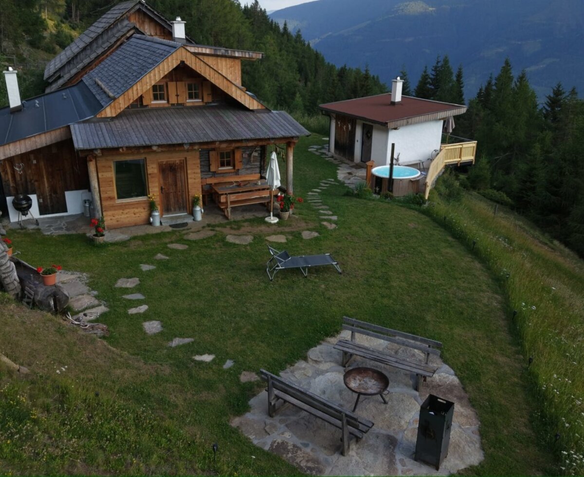 The inviting Alm featuring a well-kept garden, a cozy fire pit area, and an outdoor hot tub surrounded by picturesque mountain scenery.