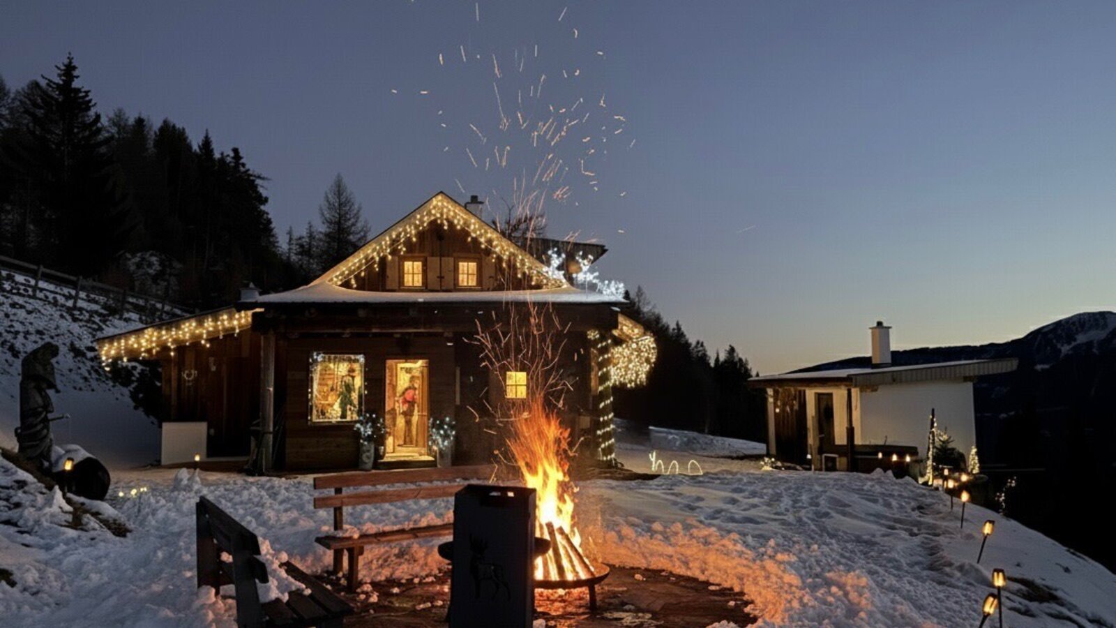 A winter evening at the hut: a crackling fire, soft festive lights and the snow-covered mountain scenery create a special atmosphere.