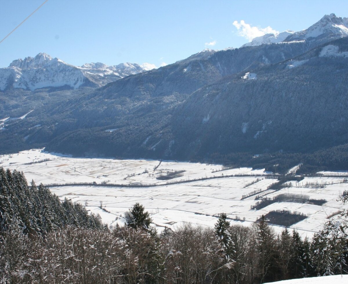 View of the snow-covered mountain range and valley, with forests and fields, from the Alpine Hut.