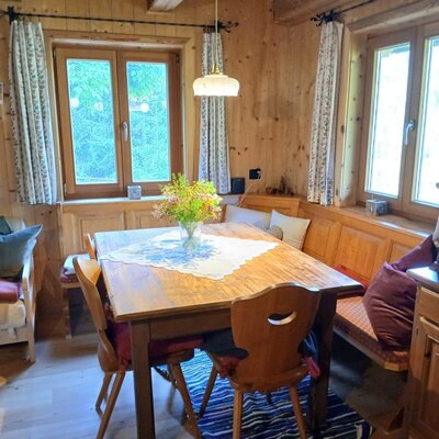 Dining area with a wooden table, corner bench, and chairs, surrounded by wooden walls and windows.