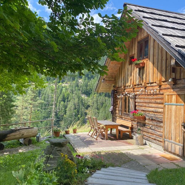 The exterior of the Bed and Breakfast, featuring a wooden facade, a paved outdoor seating area, and views of the forested mountain landscape.