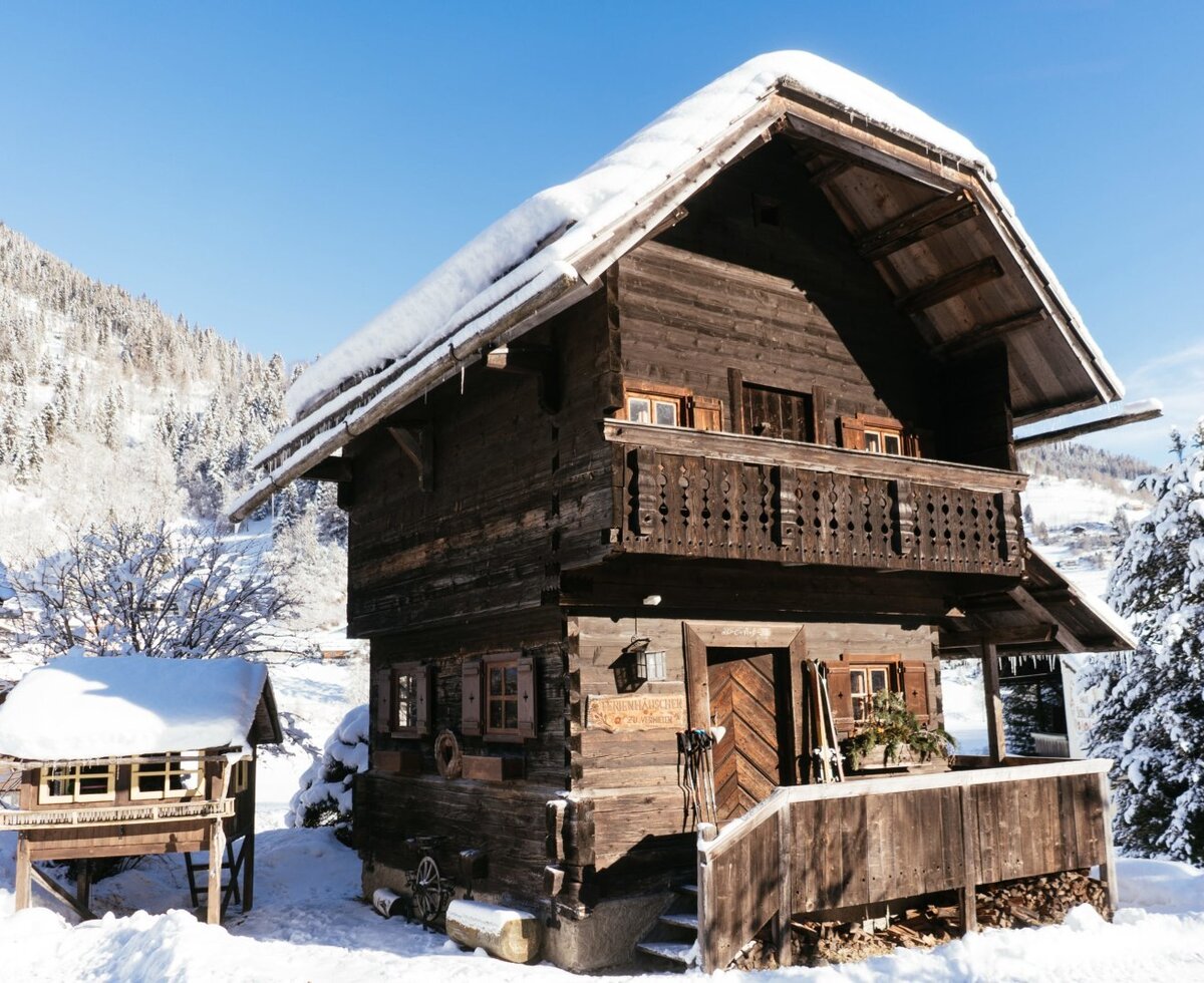 The wooden Farm House exterior, featuring a snow-covered roof and a balcony, surrounded by a snowy winter landscape.