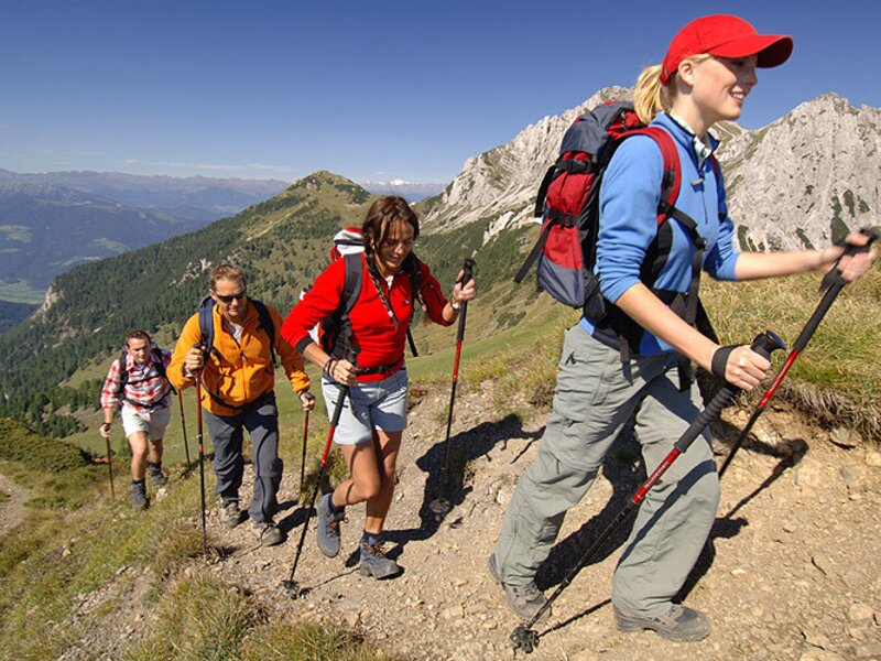 Guests hiking a mountain trail with trekking poles, illustrating outdoor activities available from the Farm House.