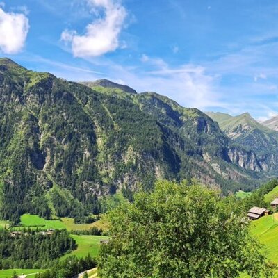 The farmhouse is situated in a mountain landscape with green slopes, offering a wide view over the valley.