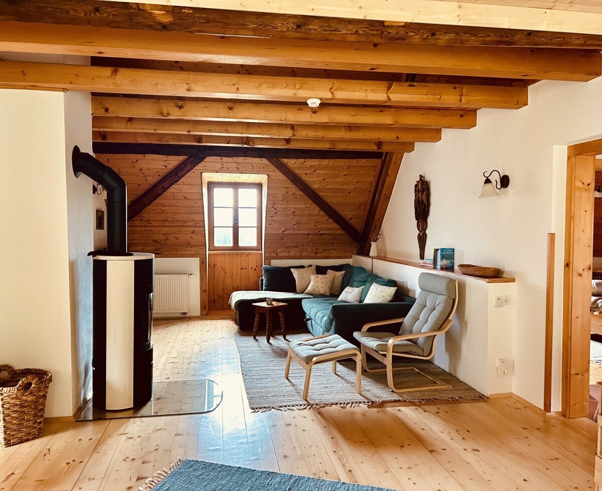The living area of the vacation rental includes a wood-burning stove, a corner sofa, an armchair, and exposed wooden ceiling beams.