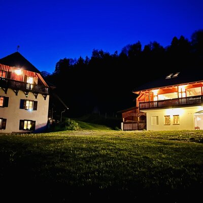 The two vacation rentals illuminated at night, one featuring traditional architecture with a balcony, and the other with a large balcony and an integrated garage.