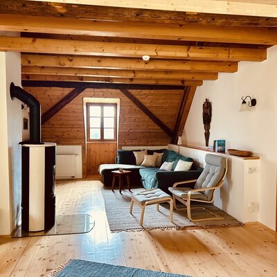 The living area of the vacation rental includes a wood-burning stove, a corner sofa, an armchair, and exposed wooden ceiling beams.