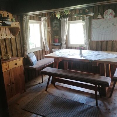 The Alpine Hut's dining area includes a large wooden table with cushioned benches, wooden wall paneling, and multiple windows.