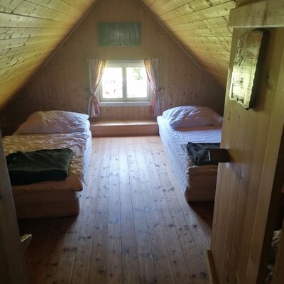 Sleeping area in the Alpine Hut with two single beds, wooden paneling, and a window.