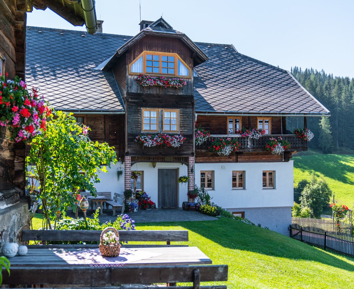 The farm house with its traditional wooden architecture, balconies with flower boxes, and an outdoor seating area on the lawn.