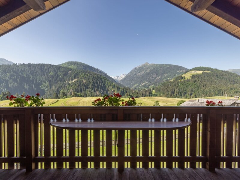 Balcony of the Farm House with a wooden railing, a small table, and flower boxes, offering a view of the Carnic Alps.