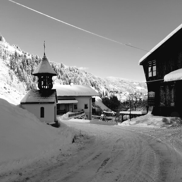 The snowy farmhouse with a small chapel and a swing set in winter.