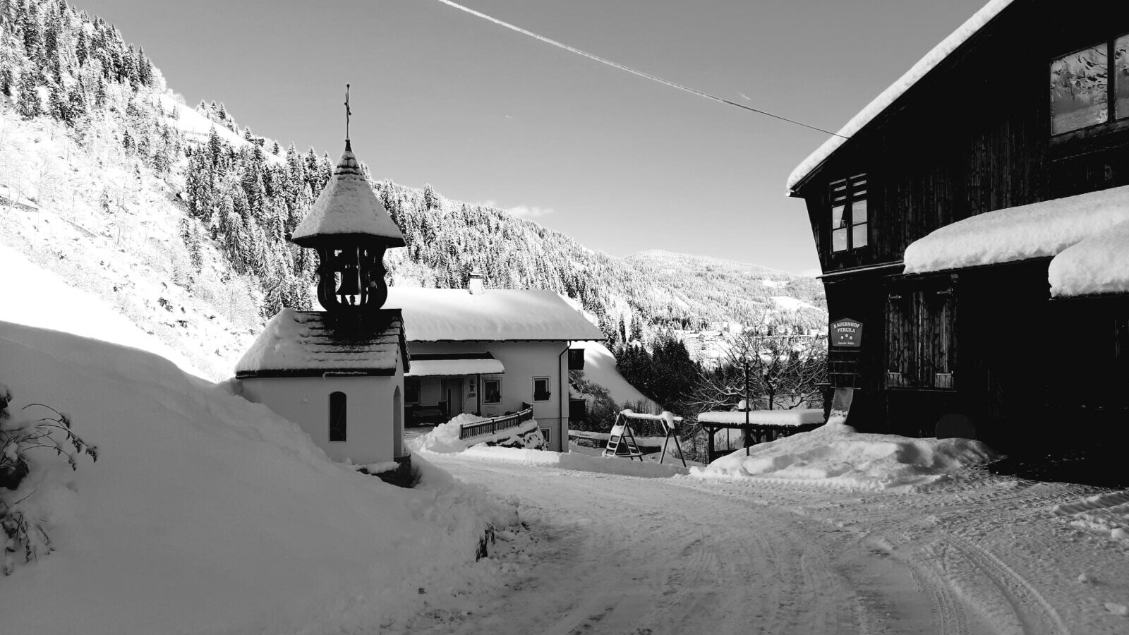 The snowy farmhouse with a small chapel and a swing set in winter.