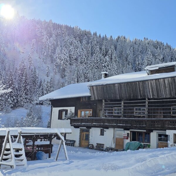 The farmhouse in a snowy winter landscape with a forest in the background and a play structure in the foreground.