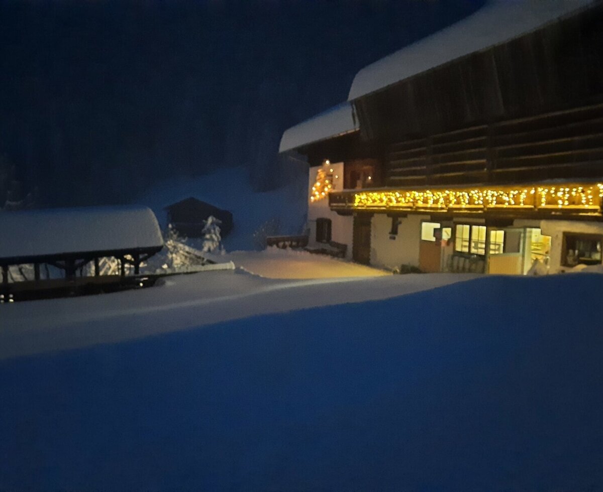 The snow-covered farmhouse at night, featuring warmly lit balconies and a thick blanket of snow.