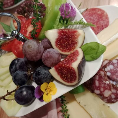 A savory platter at the Farm House featuring a selection of cheeses, sliced salami, figs, grapes, tomatoes, and cucumbers.