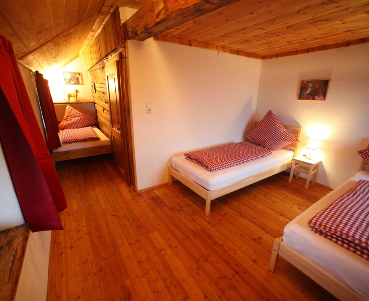 Bedroom in the farmhouse featuring three single beds, including one in an alcove, with wooden floors and ceiling.