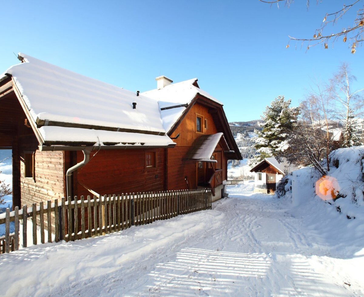 The snow-covered exterior of the farmhouse with a fenced path leading to the entrance.