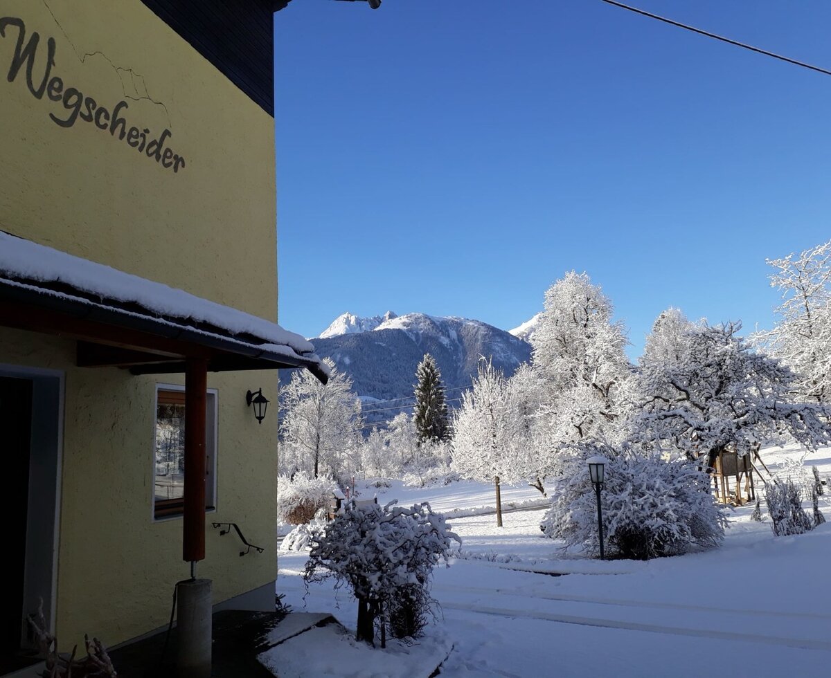 The Farm House "Wegscheider" surrounded by snow-covered trees and panoramic mountain views in winter.