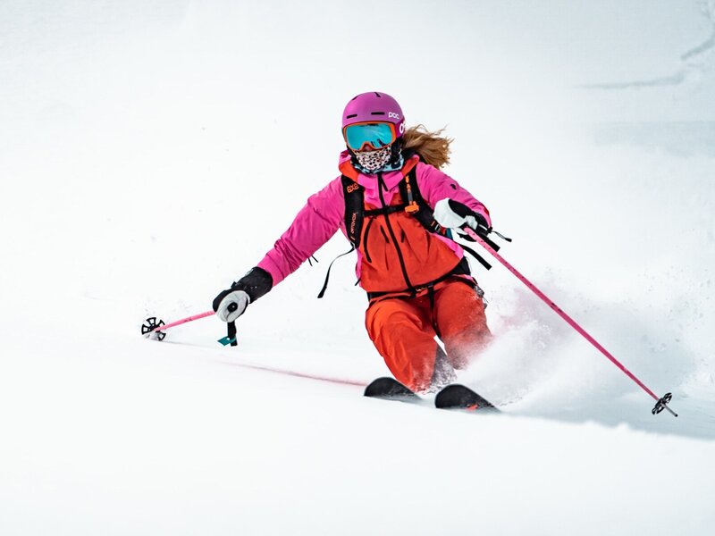 A person in pink and orange ski gear making a turn on a snow-covered slope.