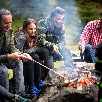 Guests roasting sausages over a campfire at the Alm.