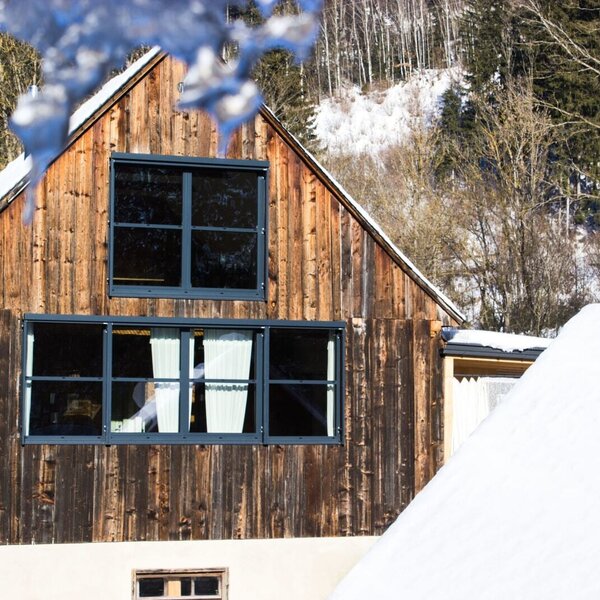 The farmhouse exterior during winter, featuring wooden siding and multiple windows.